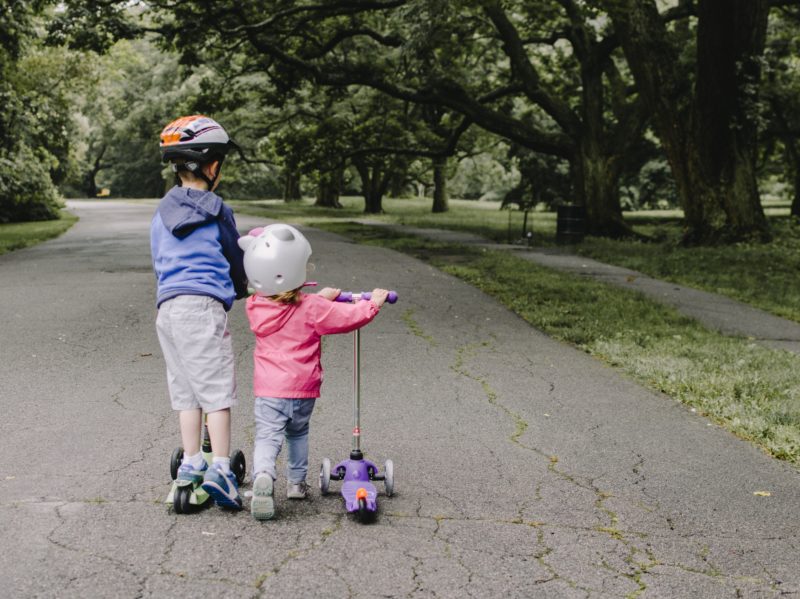 Photo of two children playing on a road with scooters; Photo by Kelly Sikkema on Unsplash